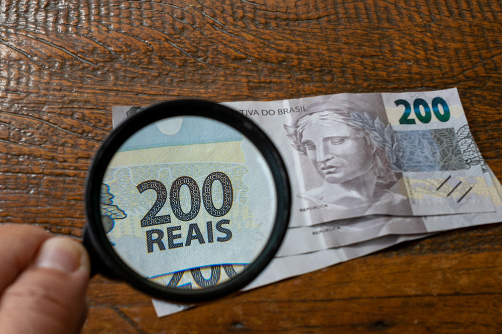 Hand With Magnifying Glass Watching New Brazilian Money Bill On - Barão Assessoria Contábil